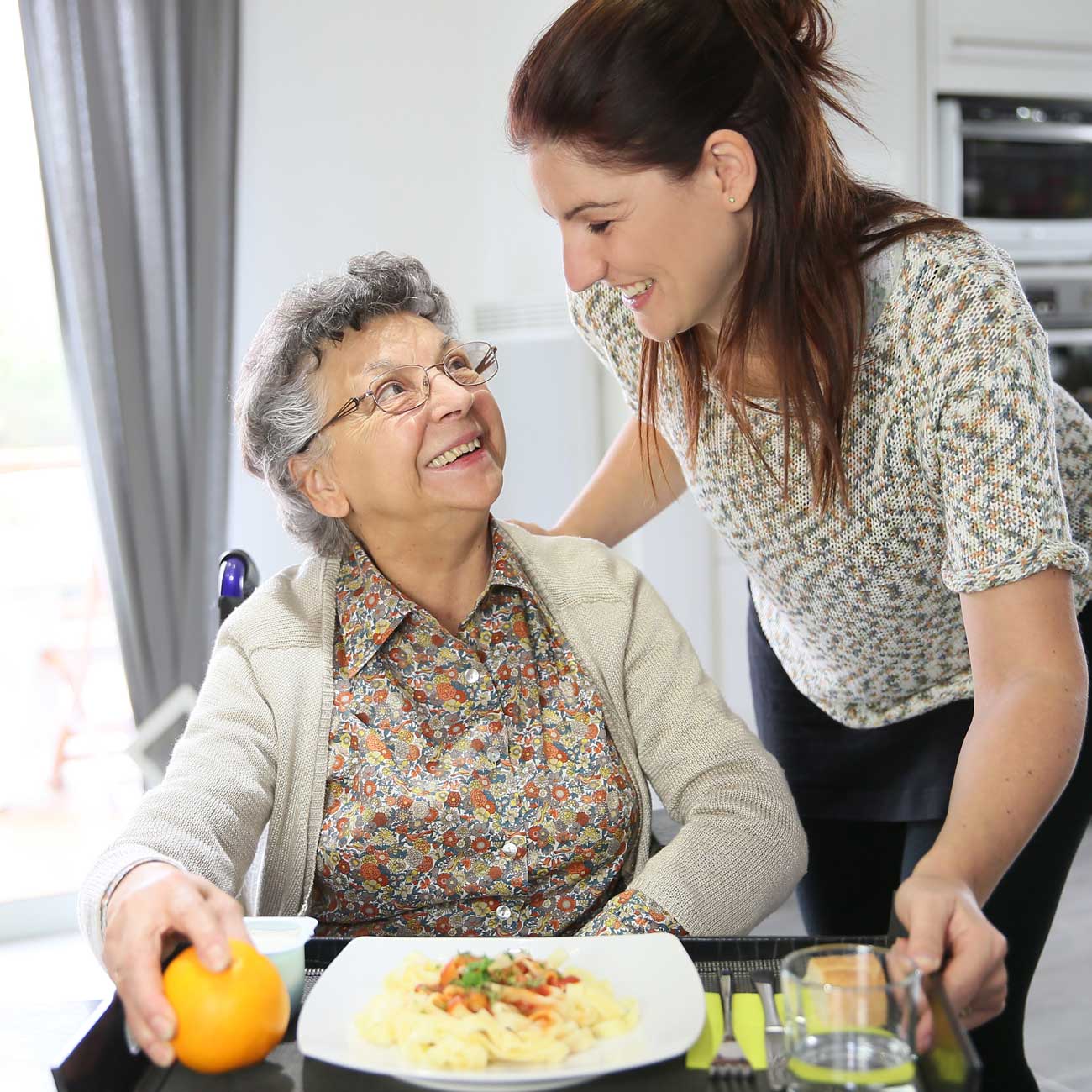 Private-duty caregiver in Queens preparing a meal and offering companionship to an elderly woman at home—part of OurCare’s trusted in-home personal aide services.